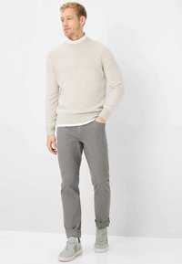 Lichtgrijze gebreide trui met geribbelde structuur, gecombineerd met lichtgrijze broek en grijze sneakers met witte zolen. Eenvoudig, modern ontwerp.