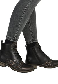 Beneden in grijze strakke spijkerbroek, zwart leren veterlaarsjes met luipaardprint stof en ritssluiting aan de zijkant.