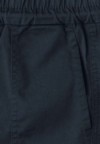 Pružný pas a detail boční kapsy na tmavě šedých bavlněných kalhotách, detailní záběr.