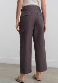 Baggy dark gray cargo pants with multiple back pockets, cropped length, and visible stitching at the hem. Worn with flat sandals.