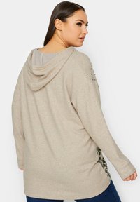 Beige hoodie met een relaxte pasvorm, zachte textuur en leoplantenaccenten aan de zijkanten. Bevat decoratieve studs op de schouders.