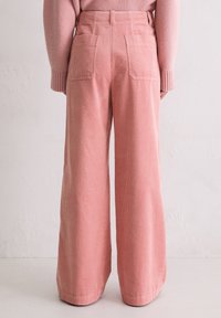 Szerokie spodnie ze sztruksu w miękkim różowym kolorze, z pionowymi prążkami, wysokim stanem, tylnymi kieszeniami i gładką fakturą.