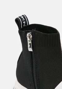 Czarny dziany botek do kostki z bocznym zamkiem i zawieszką do ściągania. Wzór obejmuje prążkowaną fakturę z białym akcentem w postaci logo.