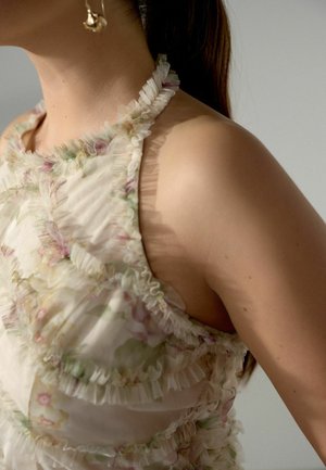 Frau trägt ein ärmelloses, geblümtes Kleid mit gerafften Kanten und goldenen Creolen, zeigt Oberkörper und Hals.