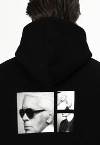 Hoodie preta com três imagens impressas em preto e branco: uma de uma pessoa de óculos de sol, as outras duas mostram perfis de indivíduos.