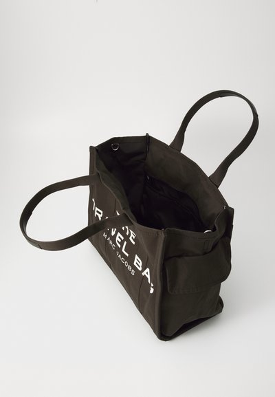 Borsa da viaggio in tela di colore verde scuro con due manici, apertura superiore e testo stampato bianco su un lato. Presenta un ampio interno senza scomparti.