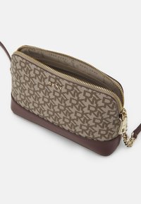 Torebka na ramię DKNY z brązowym wzorzystym materiałem, złotym zamkiem błyskawicznym, ciemnobrązową skórzaną podstawą oraz odpinanym łańcuszkowym paskiem. Wnętrze wyłożone materiałem.