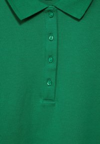 Grön polotröja med texturerad tyg, en krage och sex matchande knappar längs framknäppningen.