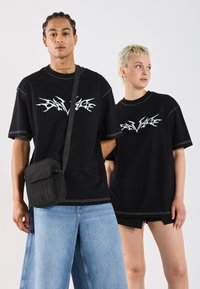 Sorte oversized T-skjorter med hvitt grafisk logo, kombinert med lyseblå baggy jeans og en liten svart crossbody-veske.