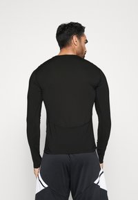 Schwarzes Langarmshirt mit Rundhalsausschnitt und Flachnähte, aus weichem, elastischem Material gefertigt. Gestylt für einen figurbetonten, sportlichen Look.