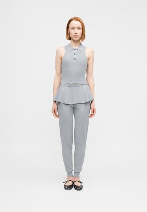 Top polo grigio senza maniche con bottoni, abbinato a un pantalone grigio a gamba affusolata e ballerine nere. Tessuto liscio, design aderente con vita svasata.