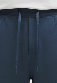 Close-up van donkerblauwe joggingbroek met zwarte elastische tailleband en bijpassende blauwe trekkoorden die van de voorkant hangen.