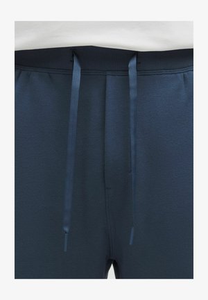 Lähikuva tummansinisistä collegehousuista, joissa on musta joustava vyötärönauha ja siihen sopivat siniset nyörit roikkumassa edestä.