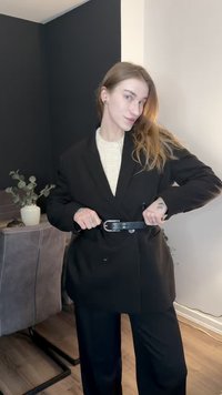 Blazer noir oversize avec boutons croisés, ceinturé à la taille. En dessous, un pull crème texturé est visible.