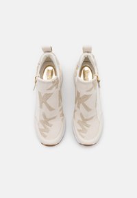 Scarpe slip-on beige in tessuto lavorato a maglia con motivo di logo metallico dorato. Dotate di chiusura con zip e suola in gomma bianca.