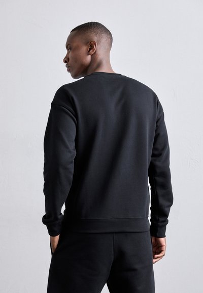 Sudadera negra con cuello redondo, puños de canalé y cintura elástica. Textura suave sin logotipos ni patrones visibles, diseño ceñido.