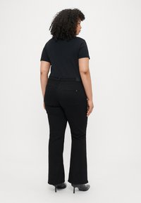 Jean évasé noir et t-shirt noir ajusté. Les jeans présentent un design classique à cinq poches et sont fabriqués en denim. Texture lisse.