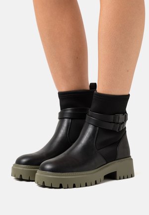 Schwarze Knöchelstiefel mit einer glatten Lederoberfläche und Gummisohle. Mit elastischen seitlichen Einsätzen, doppelten Schnallenakzenten und einer strukturierten Sohle.