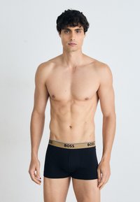 Schwarze Boxershorts mit einem goldenen und schwarzen "BOSS"-Logo-Bund. Hergestellt aus glattem Stoff, bieten sie ein enganliegendes Design für höchsten Komfort.