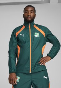 Green and orange windbreaker with a high collar, zip fastening, and logo. Features smooth texture and contrast side panels.