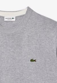 Grijze sweatshirt met een ronde hals, geribde manchetten en een klein groen Lacoste krokodillenlogo aan de linkerkant. Comfortabele gebreide textuur.