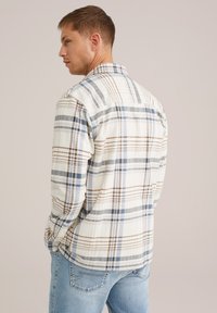 Flannel shirt in off-white with blue and brown plaid pattern. Long sleeves, button-down collar, textured fabric, and back yoke detail.