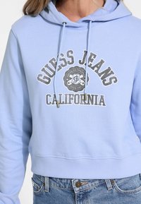 Cropped hoodie azzurro chiaro con stampa del logo frontale, cordini e orlo a coste. Abbinato a pantaloni shorts di jeans a vita alta.