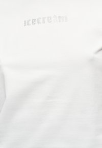 Λευκό ύφασμα με μικρές ασημένιες στρας, τοποθετημένες ώστε να σχηματίζουν τη λέξη "icecream" κοντά στο πάνω κέντρο.