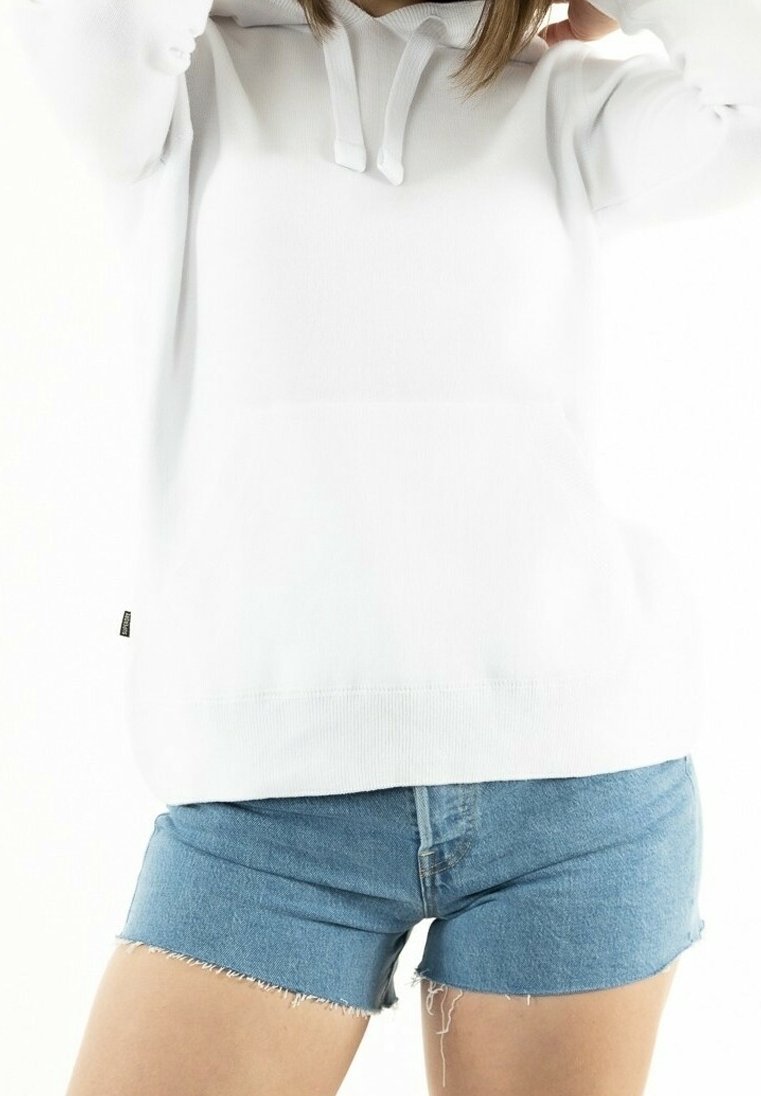 Persona che indossa una felpa bianca con cappuccio e cordini, insieme a pantaloni corti in denim azzurro chiaro con bordi sfrangiati, su uno sfondo bianco.