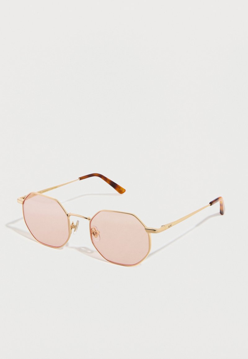 Occhiali da sole ottagonali con montatura in metallo dorato, lenti sfumate rosa e estremità delle aste in tartaruga, esposti su una superficie bianca.