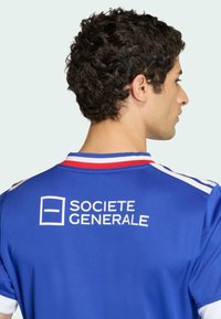 Modrý sportovní dres s bílými detaily. Má kulatý výstřih, krátké rukávy a na zadní straně je potisk s logem "SOCIETE GENERALE".