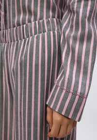 Tela de rayas grises y rosas con textura suave. Puño visible con detalle de costura. Cintura elástica y diseño ajustado.