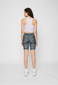 Top scurt mov deschis cu design racerback, asortat cu pantaloni scurți de biciclist verde închis cu model și adidași albi.