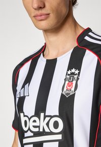 Mustvalge triibuline spordisärk kerge kangaga, millel on punased aktsendid, tikitud logo ja julge "beko" embleem.