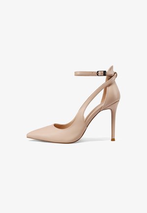 Scarpa beige con tacco alto e punta appuntita, cinturino sottile alla caviglia e design laterale traforato su sfondo bianco.