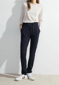 Marineblaue Jogginghosen mit elastischem Bund und Kordelzug. Kombiniert mit einem leichten Strickpullover. Weiße Sneaker mit roten Akzenten.