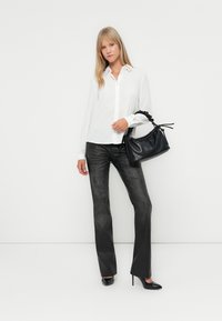 Witte button-up shirt, zwarte broek en zwarte hoge hakken. Zwarte handtas met textuur en een geplooide handgreep. Eenvoudig, modern ontwerp.