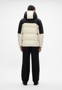 Pufferjakke med en cremefarvet front, sorte skuldre og hætte. Tekstureret, quiltet design med en afslappet pasform, parret med brede sorte bukser.
