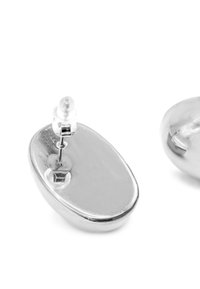 Orecchini ovali in argento con una finitura lucida. Presentano una chiusura a perno e bordi lisci e curvi. La riflessione della luce crea sottili riflessi.