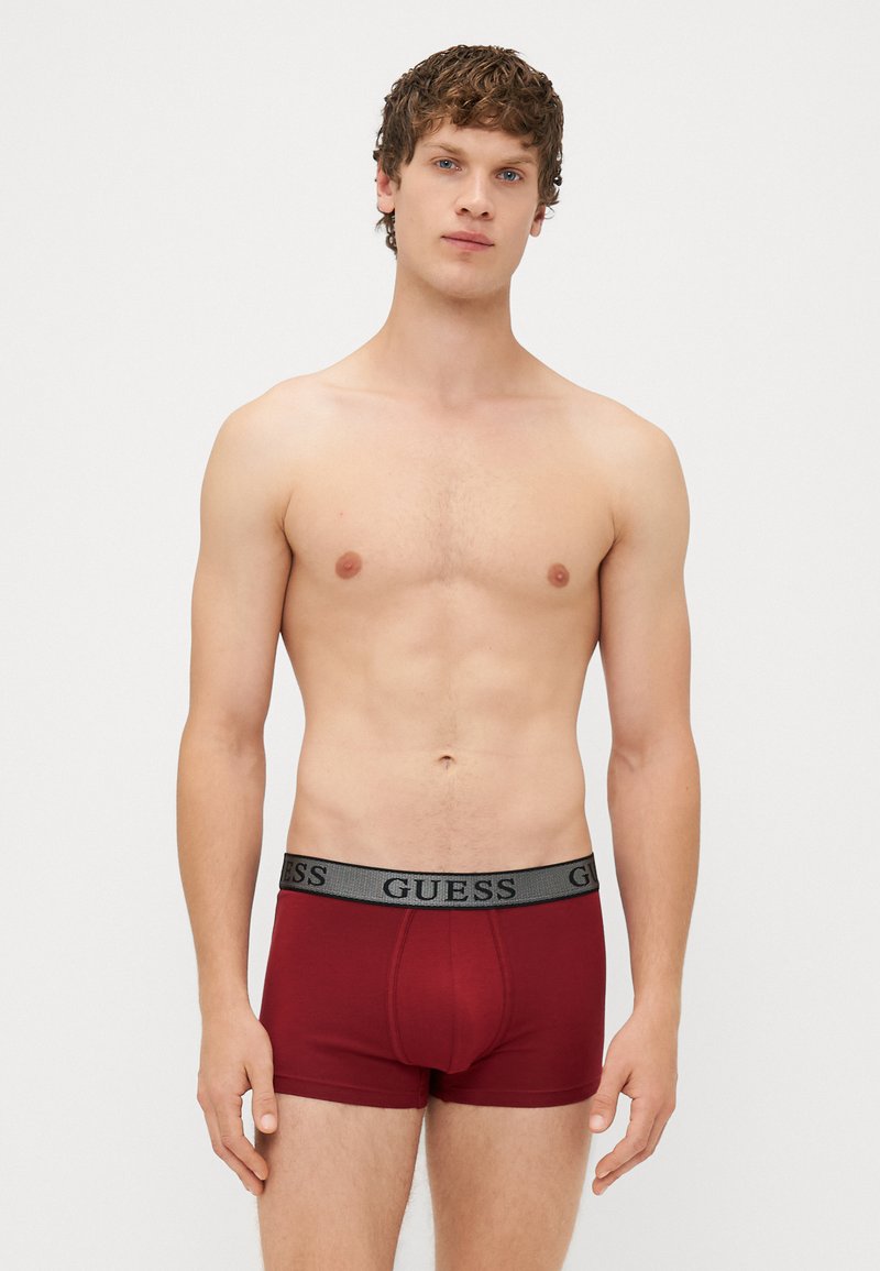 Boxer da uomo rossi in cotone con una cintura elastica grigia che presenta in modo evidente il logo "GUESS" sul davanti.