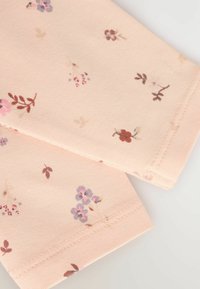 Tissu rose clair avec de petits motifs floraux dans des teintes de violet, rouge et marron. Présente des coutures soignées le long des bords.