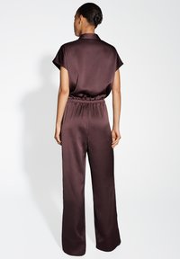 Combinaison en satin bordeaux avec un col, des manches courtes, une taille élastique et un pantalon à jambes larges avec une finition texturée.