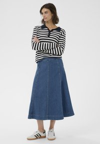 Gestreepte zwart-witte blouse met lange mouwen en kraag, gecombineerd met een blauwe denim maxirok en witte sneakers met zwarte strepen.