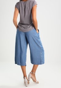 Gråmönstrad kortärmad topp i kombination med blå denim culotter, med en lös passform och sidofickor, kompletterad med ljusgrå klackar.