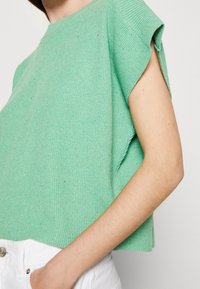 Zielony prążkowany żakiet z krótkimi rękawami i wysokim kołnierzem, o luźnym kroju i widocznymi detalami tekstury.