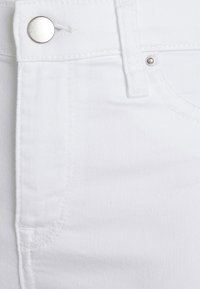 La tela de denim blanca presenta una vista en primer plano de un botón y el detalle de la costura, mostrando una textura suave y un diseño limpio y simple.