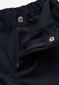 Pantalon bleu marine avec une taille partiellement dézippée et deux boutons-pression en métal de chaque côté de l'ouverture.