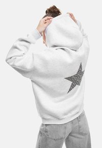 Grijze hoodie van zachte stof met een zwart luipaardprint ster ontwerp op de achterkant. Heeft een ruime capuchon en geribbelde manchetten.