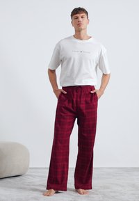 Pantalons de détente à carreaux rouges avec une taille élastique, associés à un t-shirt à manches courtes blanc arborant un petit logo sur la poitrine.
