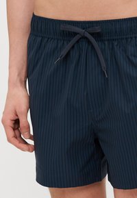 Pantaloni da mare a righe blu realizzati in tessuto liscio. Presentano un cinturino elastico con lacci per la regolazione.